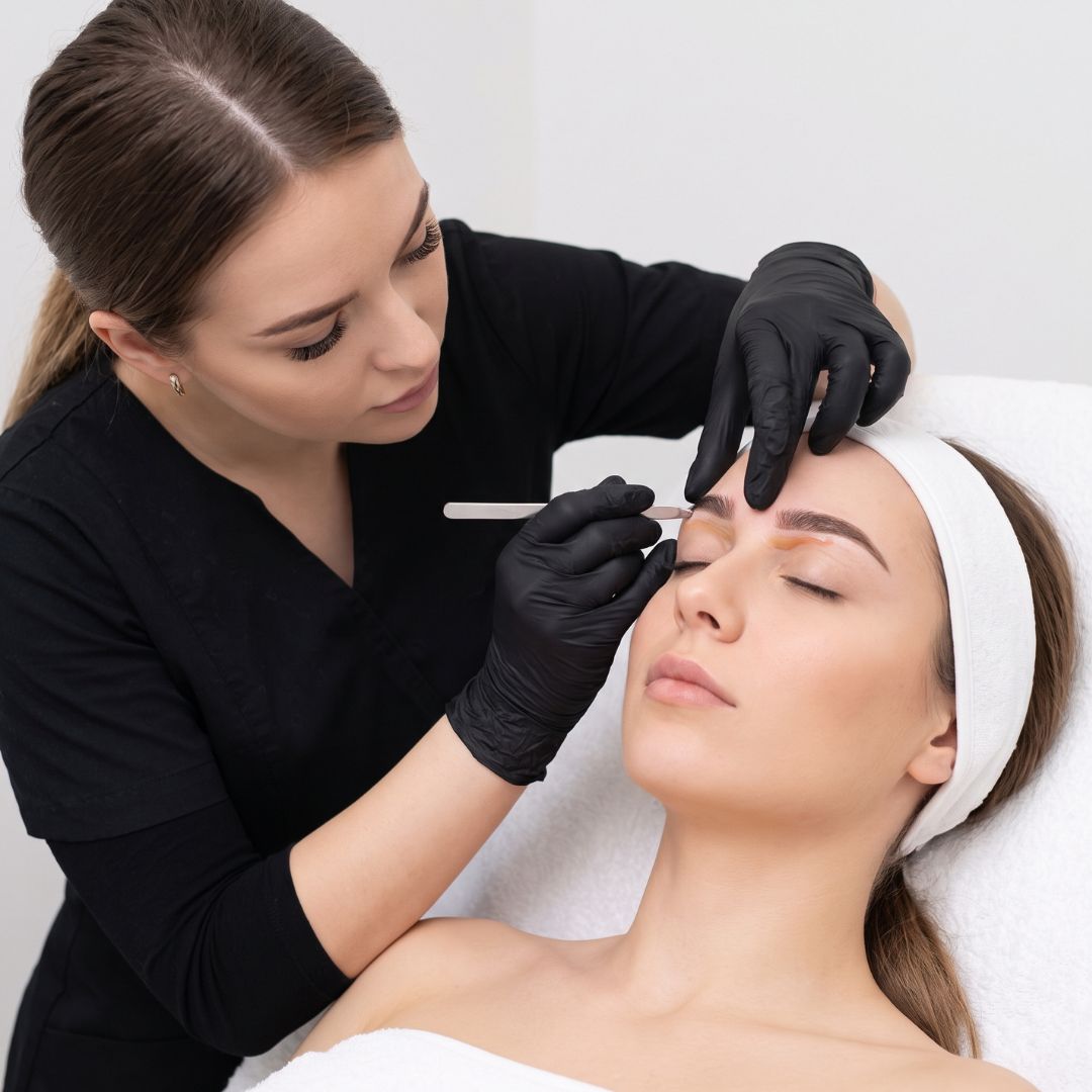 Close-up of an esthetician in black gloves carefully shaping a client's eyebrow using warm wax.