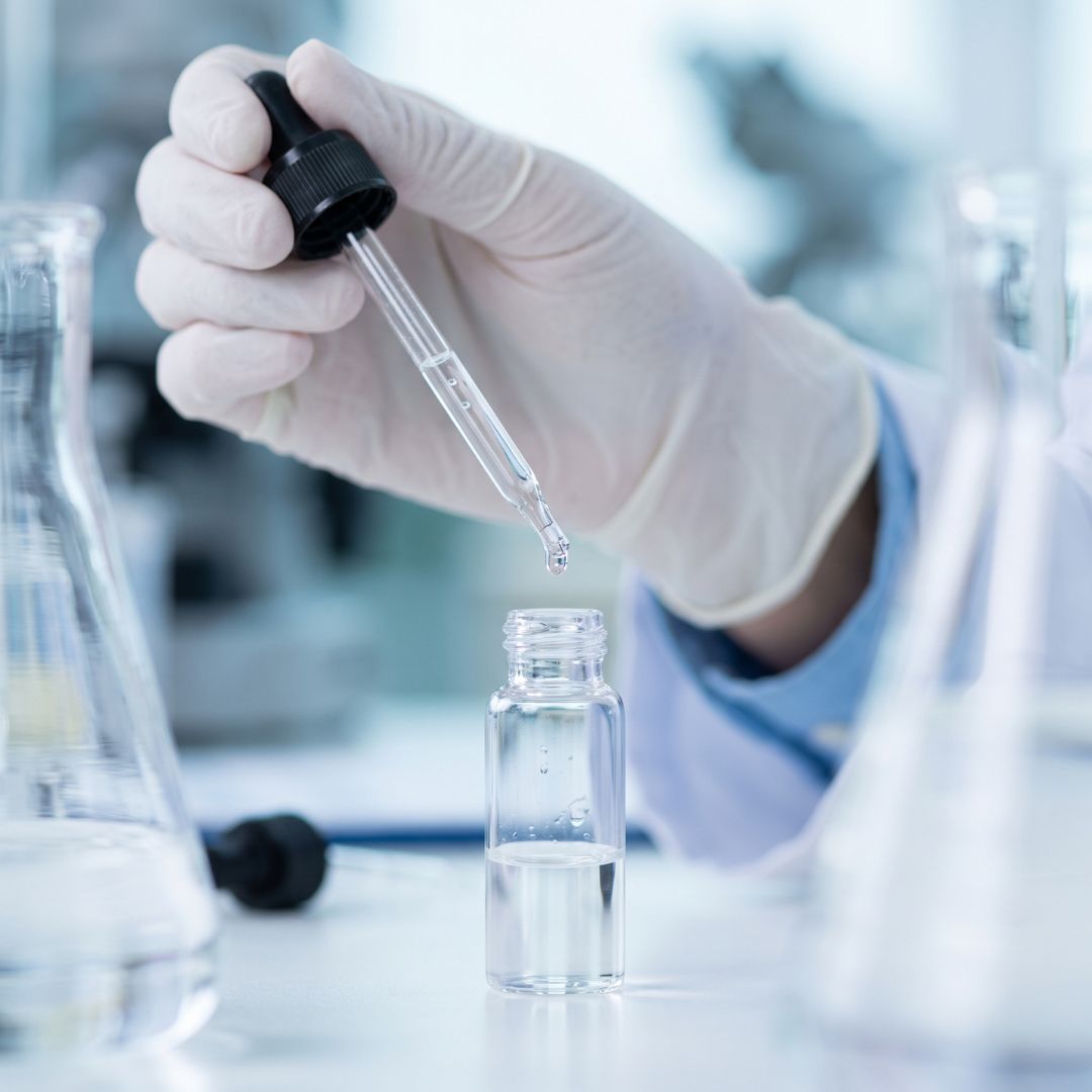 Close-up of a scientist's gloved hand formulating a clear skincare serum.